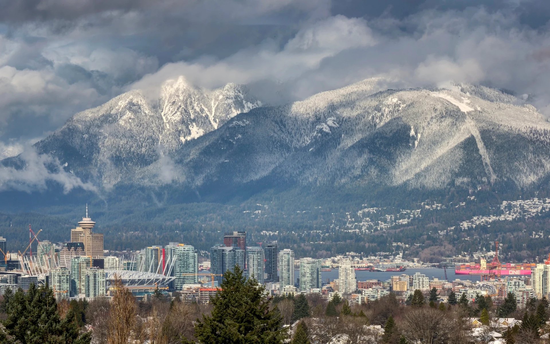 Snow-dusted North Shore mountains rising over Burrard Inlet, with North Vancouver's shoreline homes on the slopes